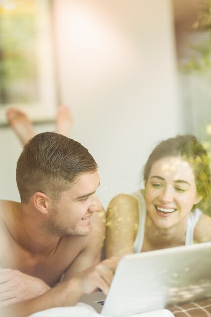 Cute couple lying on bed using laptop