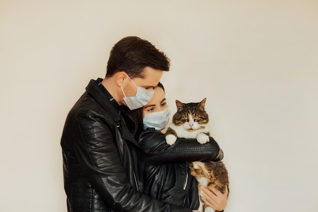 Cute couple in medical masks. Girl holding in hands his serious cat