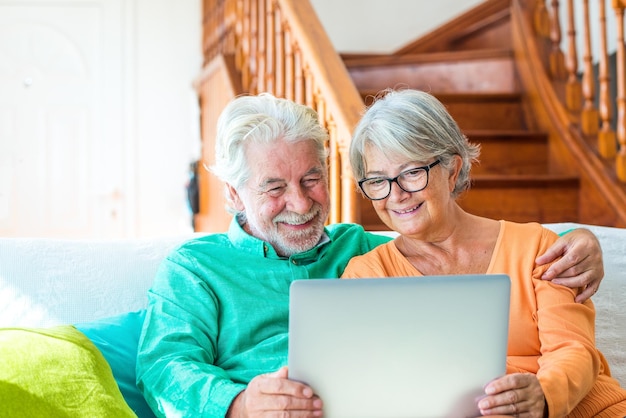 사진 소파에 함께 앉아 집에서 노트북을 사용하여 재미 있는 영화를 보는 노인의 귀여운 커플 실내에서 웃는 컴퓨터 pc를 들고 두 성숙한 연금