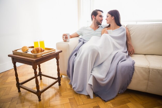 Симпатичные пары, расслабляющий на диване под одеялом