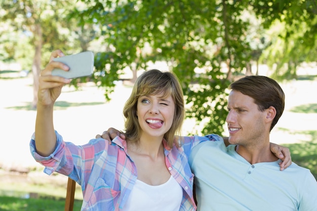 Cute couple sitting on bench in the park taking a selfie