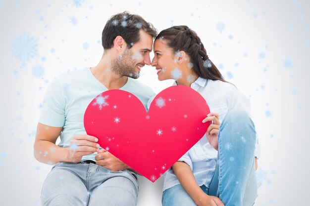 cute couple sitting holding red heart against snow falling