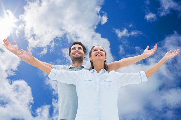 Cute couple standing with arms out against bright blue sky with clouds