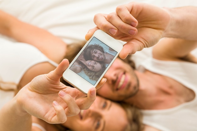 Cute couple taking a selfie lying on their bed