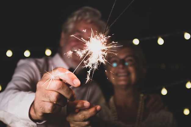 Una bella coppia di due anziani innamorati insieme la notte di capodanno che giocano con le stelle filanti in mano vicino alla telecamera