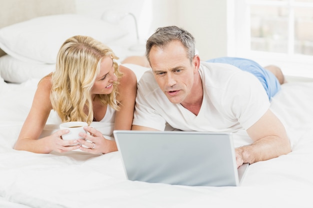 Cute couple using laptop in bed in their bedroom