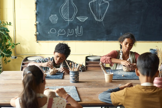 Photo cute creative schoolkids sculpting clay mugs or bowls