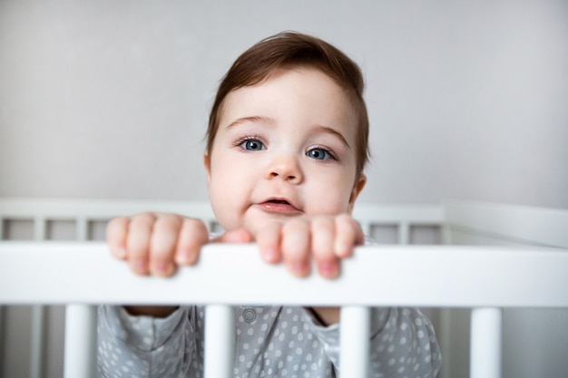 Cute curious baby standing in a white crib bed.