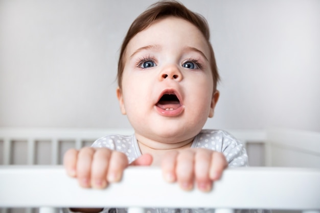 Cute curious baby standing in a white crib bed.