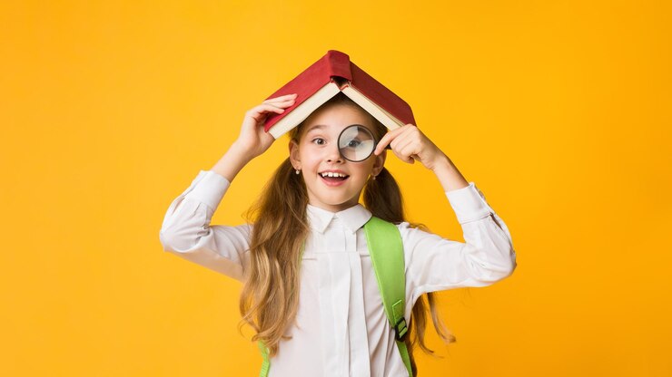 Photo cute curious schoolgirl looking through magnifier covering head with book