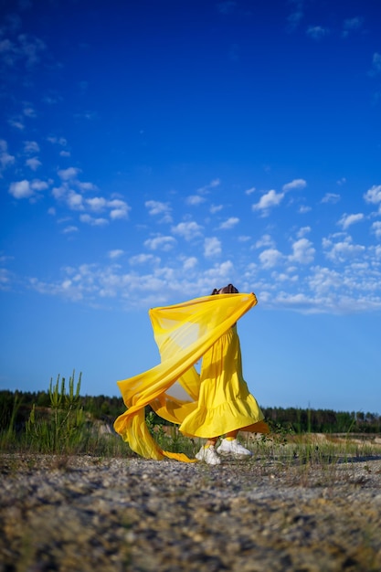 Cute curly beautiful blonde girl in a yellow summer dress in nature