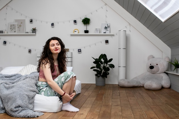 Photo cute curly girl waking up sleepy in the morning and enjoying the start of the new day. she is smiling while sitting the edge of the bed which laid directly on the wooden floor.