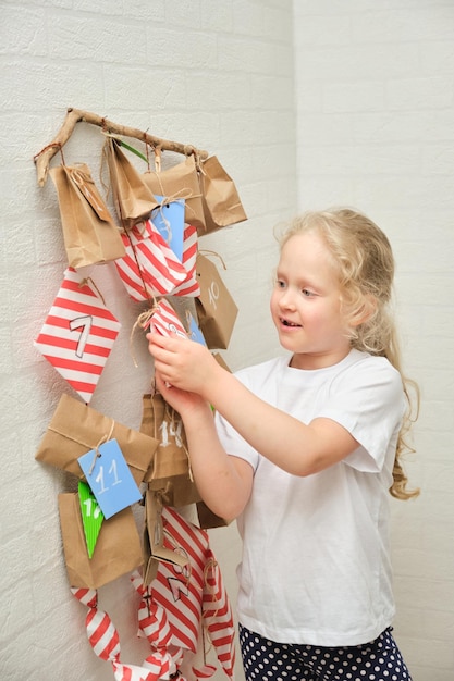 Cute curly girl with blond hair and a girl and an anvent calendar hanging on the wall the eve of christmas