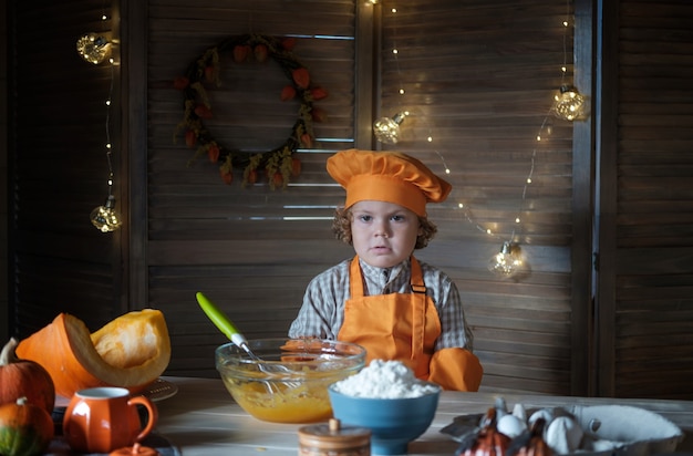 Foto il simpatico ragazzo dai capelli ricci in un costume da cuoco arancione sta preparando la torta di zucca per il ringraziamento. tradizioni di vacanza in famiglia