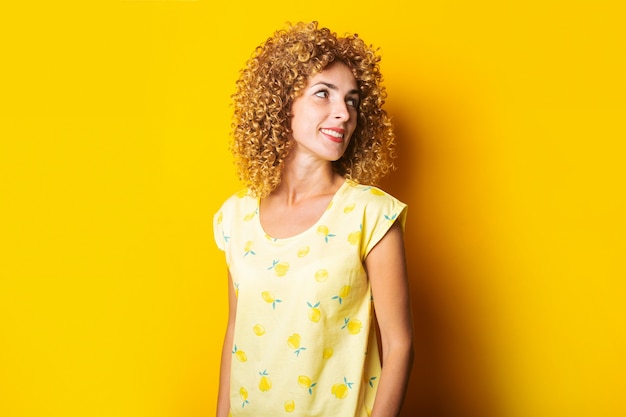 Cute curly-haired girl smiling looks to the side on a yellow background