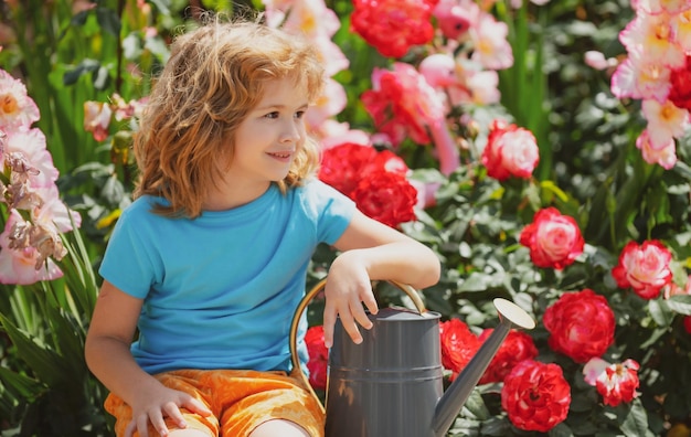 정원에서 일하는 여름 드레스를 입은 귀여운 곱슬곱슬한 어린 소년 아이가 꽃에 물을 주며 정원 가꾸기