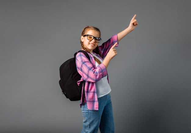 Cute cute attractive cheerful blonde schoolgirl pointing with two fingers looking to the side