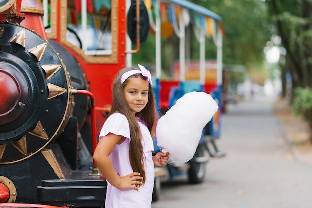 A cute darkskinned girl in a pink dress holds cotton candy in her hands in the summer in the park