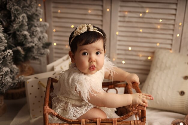 Cute darkskinned girl sitting in a wooden crib on a background\
with garlands