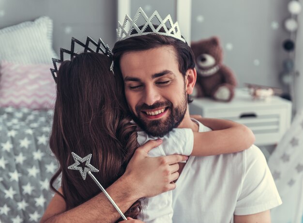 Cute daughter and her handsome dad in crowns are hugging.