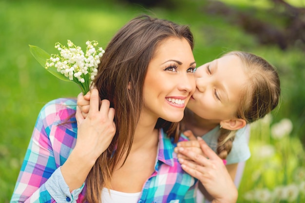 Foto figlia carina che bacia la sua mamma felice e regala al suo bouquet il mughetto per la festa della mamma nella natura.