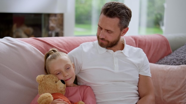 Cute daughter sitting on couch with father Cheerful man looking at small girl