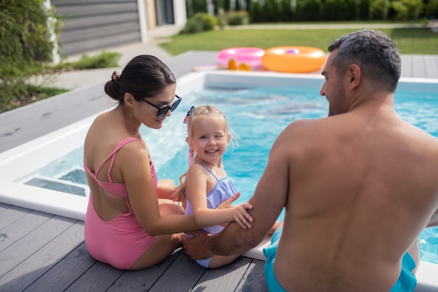 Cute daughter smiling. Lovely cute daughter smiling while resting near pool with mom and dad