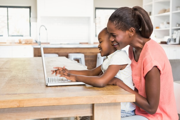 Cute daughter using laptop at desk with mother