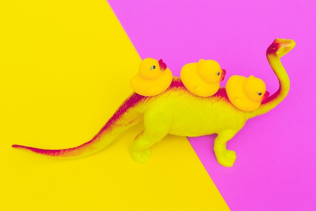 Cute Dinosaur toy and ducklings on colored background. Minimal flat lay art.