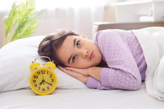 A cute disgruntled brunette in  polka dot pajamas lies on a pillow on the bed in the morning