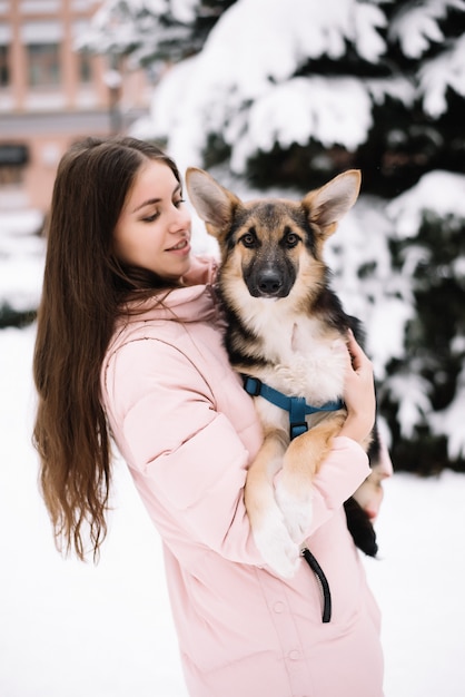 Cute dog sitting on the hands of a girl and looking at camera in snow winter