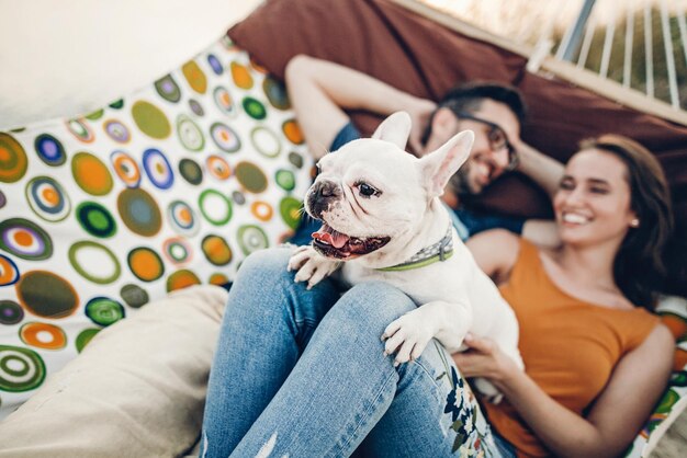 Photo cute dog smiling while on a trip with his owners joyful young family man and woman lying in comfortable hammock on a beach