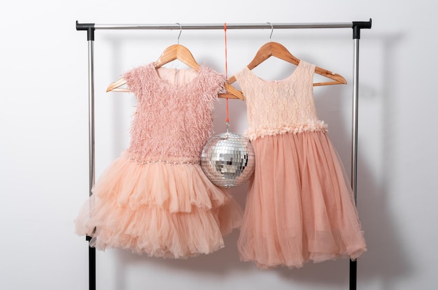 Photo cute dresses hang on hangers on clothes rail with disco ball on white wall background