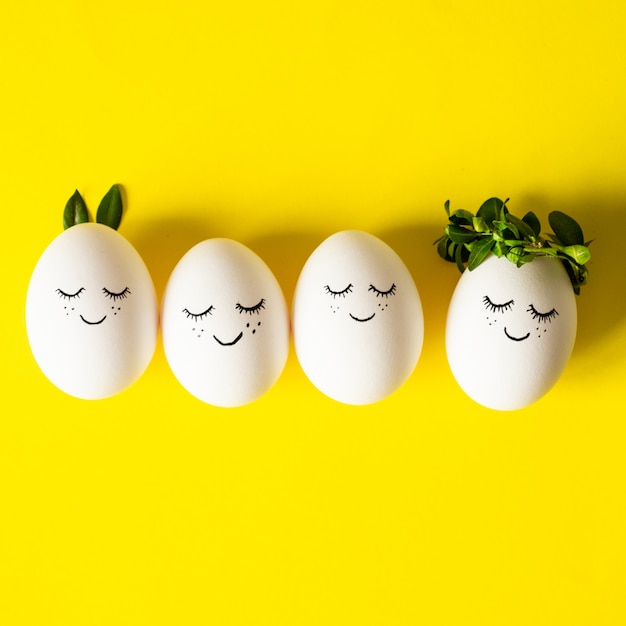 Cute Easter eggs with a painted face in a spring leaves on yellow background. Happy Easter.