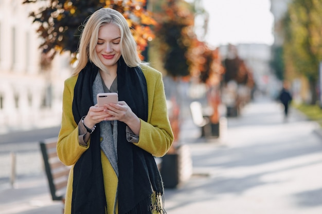 Cute emotional attractive blonde woman in coat with smartphone walks the city street. communication during the walk, lifestyle, street