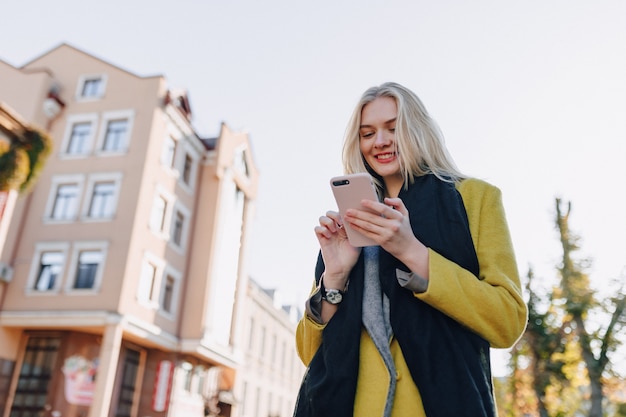 Cute emotional attractive blonde woman in coat with smartphone walks the city street. communication during the walk, lifestyle, street.