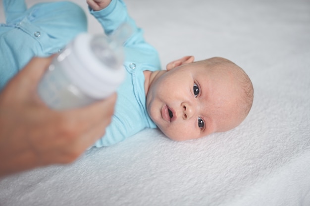 Cute emotional funny newborn boy laying on bed with milk bottle Baby facial expressions