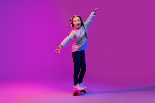 Cute emotional little girl skateboarder practicing skills on futuristic background