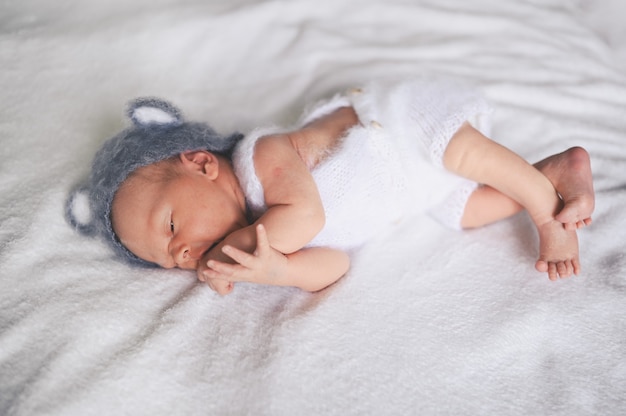 Cute emotional newborn little baby boy sleeping in crib in a knitted suit with ears.