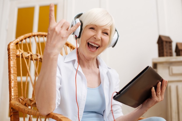 Cute enthusiastic expressive lady being rather emotional while listening to some music using her tablet