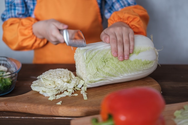 귀여운 유럽 소년 야채 샐러드 도마에 칼로 배추를 자른다.