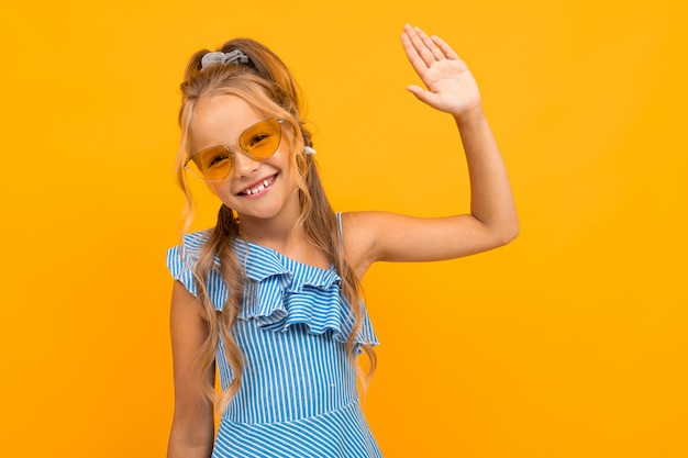 cute european girl in bright sunglasses shows a palm on a yellow wall