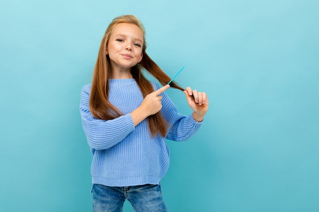 Foto ragazza europea sveglia che tiene un pettine dei capelli su blu-chiaro