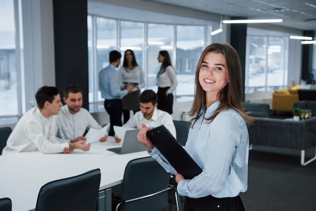 Cute european woman. Portrait of young girl stands in the office with employees at background