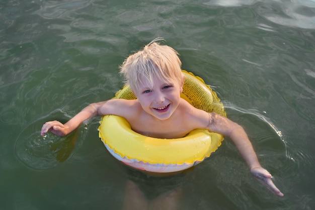 Симпатичный светловолосый мальчик плавает с резиновым кольцом Концепция безопасного отдыха на воде
