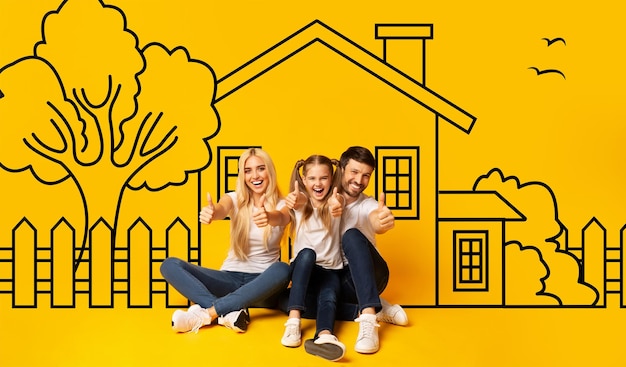 Foto famiglia carina padre madre e figlia seduti sopra disegnato su casa parete gialla mostrando pollice in su e