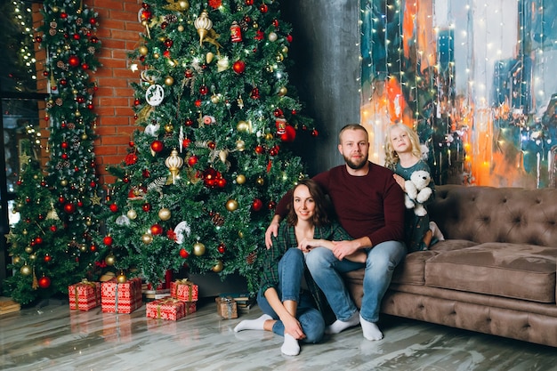 Cute family mom, dad and daughter pose at the Christmas tree