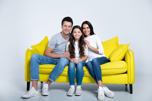 Милая семья из трех человек, сидя на желтом диване и улыбаясь, наслаждаясь своим временем вместе.