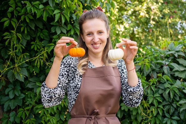 A cute farmer girl holds two small pumpkins in her hands and smiles