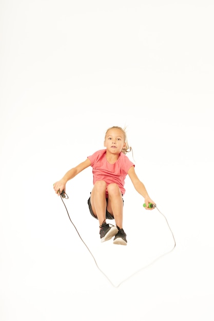 Cute female child in sportswear jumping and doing exercise with jump rope. Isolated on white background